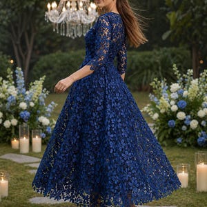May include: A navy blue midi dress featuring intricate floral lace detailing, three-quarter length sleeves, and a fitted bodice that transitions into a full, flared skirt. The garment is paired with neutral-toned pointed-toe high heels.