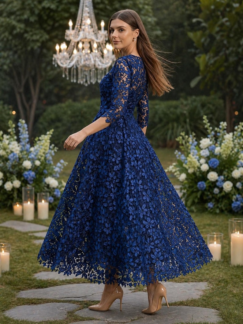 May include: A navy blue midi dress featuring intricate floral lace detailing, three-quarter length sleeves, and a fitted bodice that transitions into a full, flared skirt. The garment is paired with neutral-toned pointed-toe high heels.