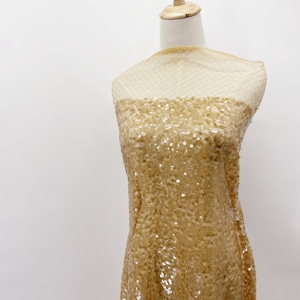 May include: Gold sequined fabric with a sheer mesh backing. The fabric is draped over a dress form.