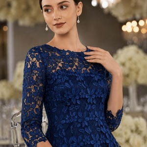May include: A dark blue dress featuring a round neckline and three-quarter length sleeves. The garment is covered in an intricate floral lace overlay with a repeating petal pattern throughout the bodice and sleeves, creating a textured appearance.