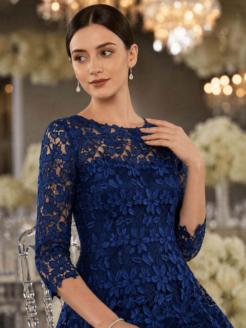 May include: A dark blue dress featuring a round neckline and three-quarter length sleeves. The garment is covered in an intricate floral lace overlay with a repeating petal pattern throughout the bodice and sleeves, creating a textured appearance.