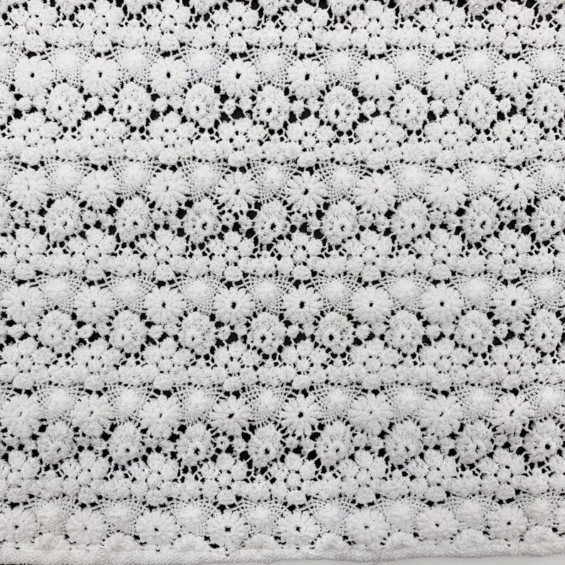 May include: White crochet fabric with a delicate floral pattern. The fabric has a textured, lace-like appearance.