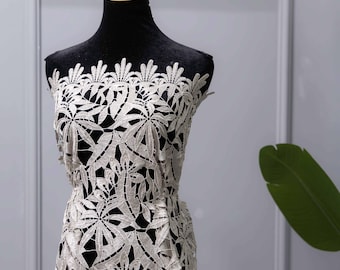 May include: Ivory lace fabric with a floral leaf pattern displayed on a black dress form. The lace is intricately designed with a repeating motif of stylized leaves. The dress form is set against a neutral gray background.