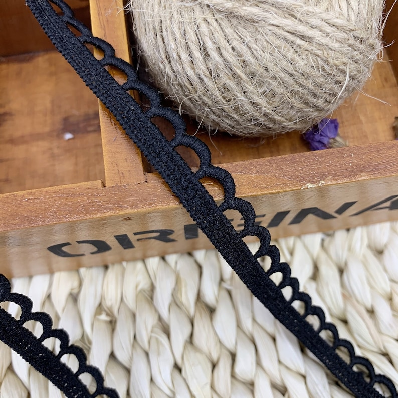May include: Black elastic trim with a scalloped edge. The trim is shown on a wooden surface.
