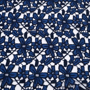 May include: A dark blue lace fabric featuring a repeating floral pattern with six-petaled flowers and small leaves connected by thin threads. The design is symmetrical and creates an openwork mesh structure with a consistent deep navy blue color.
