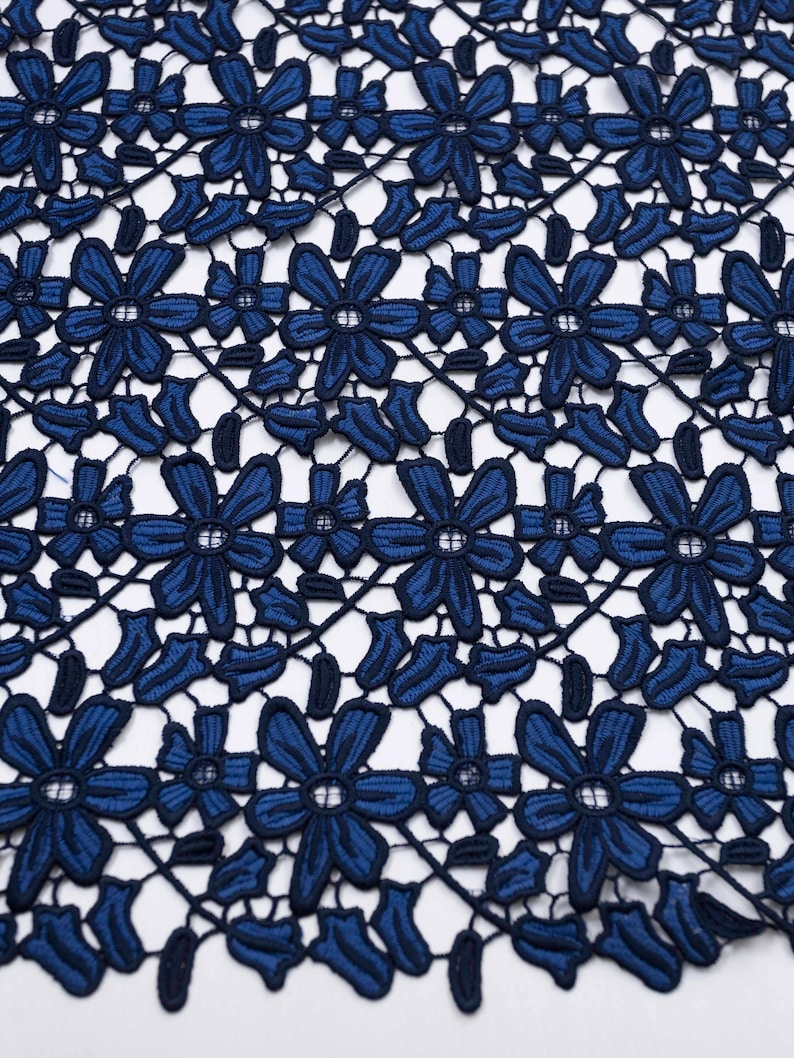 May include: A dark blue lace fabric featuring a repeating floral pattern with six-petaled flowers and small leaves connected by thin threads. The design is symmetrical and creates an openwork mesh structure with a consistent deep navy blue color.