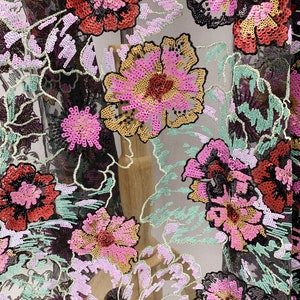Puede incluir: Tela de malla negra con dise&ntilde;os florales bordados en lentejuelas rosas, rojas, doradas y verdes.