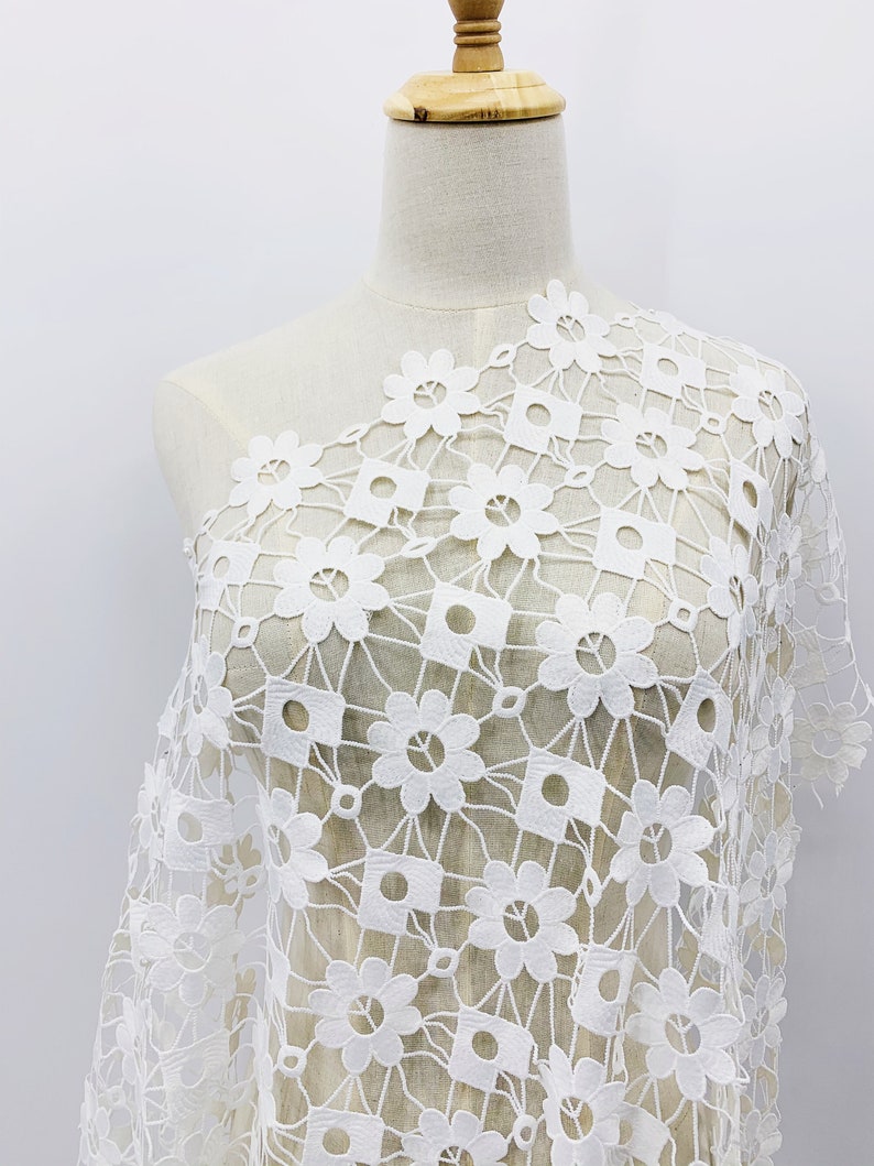 May include: White crochet fabric with a floral pattern. The fabric is delicate and has a square grid pattern with small flowers in each square.