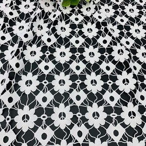 May include: White crochet fabric with a repeating pattern of peace signs and flowers. The fabric has a delicate, lacy texture.