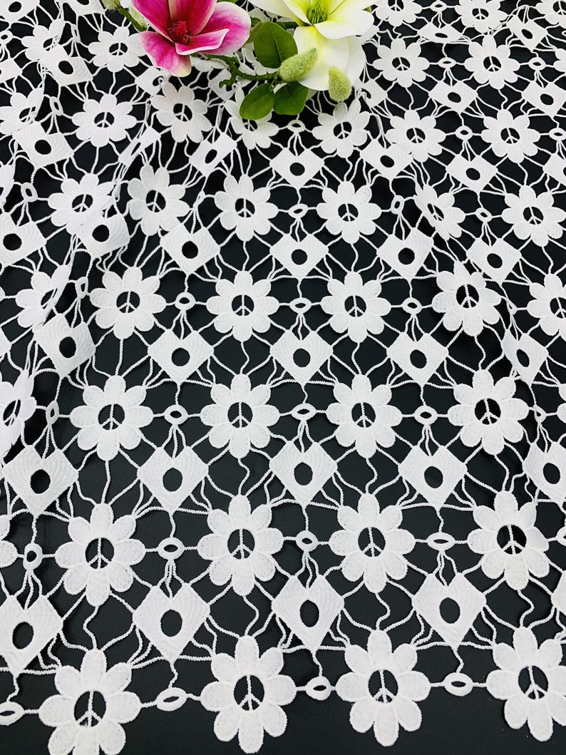 May include: White crochet fabric with a repeating pattern of peace signs and flowers. The fabric has a delicate, lacy texture.