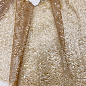 May include: A close-up of a gold sequined fabric with a delicate, sheer texture. The sequins are small and evenly spaced, creating a shimmering effect.
