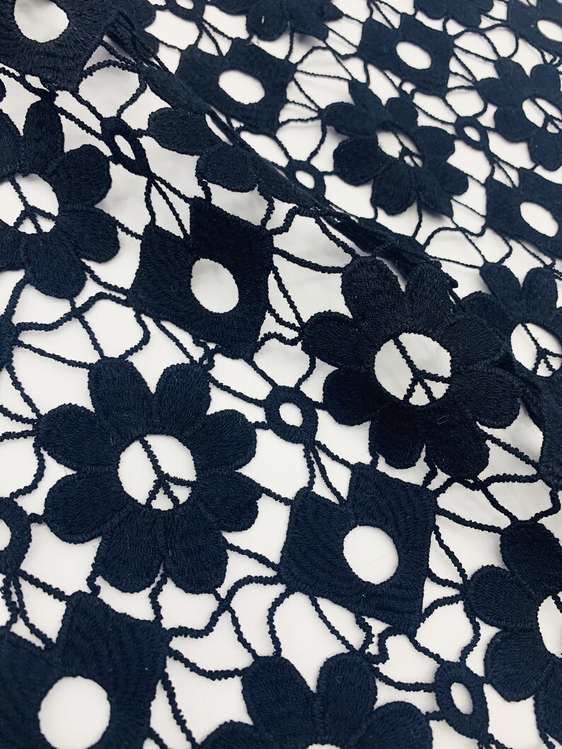 May include: Black lace fabric with a delicate floral pattern. The fabric is made of a fine mesh and has a soft, flowing texture.