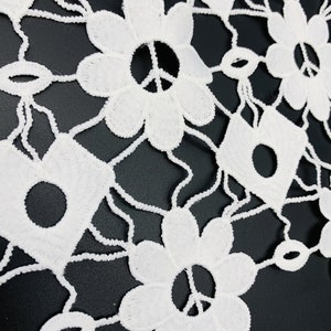 May include: White crochet lace fabric with a floral pattern featuring peace signs in the center of each flower.