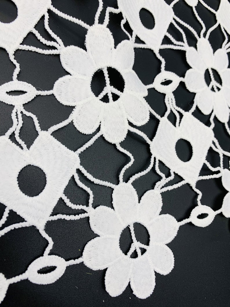 May include: White crochet lace fabric with a floral pattern featuring peace signs in the center of each flower.