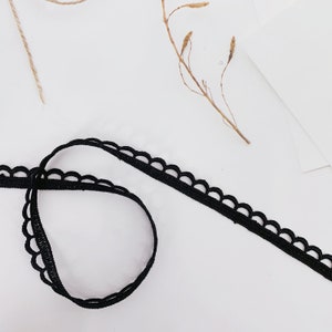 May include: Black scalloped trim lace ribbon. The ribbon is folded in half and the ends are overlapping.