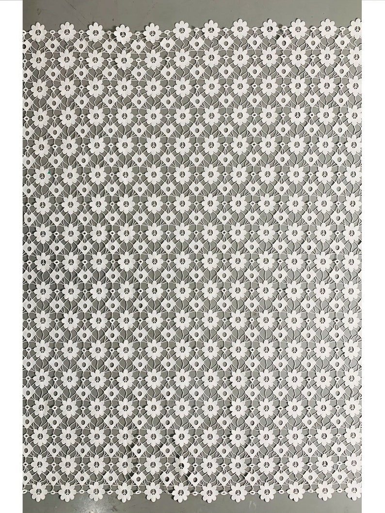 May include: White lace fabric with a repeating pattern of small flowers. The flowers have a peace sign design in the center.