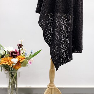 May include: Black lace maxi skirt with a floral pattern. The skirt is displayed on a wooden stand against a white background.
