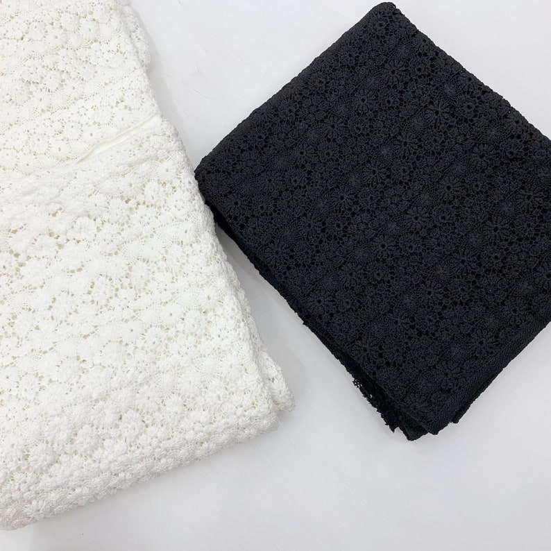 May include: Two pieces of lace fabric, one white and one black. Both fabrics have a delicate floral pattern.