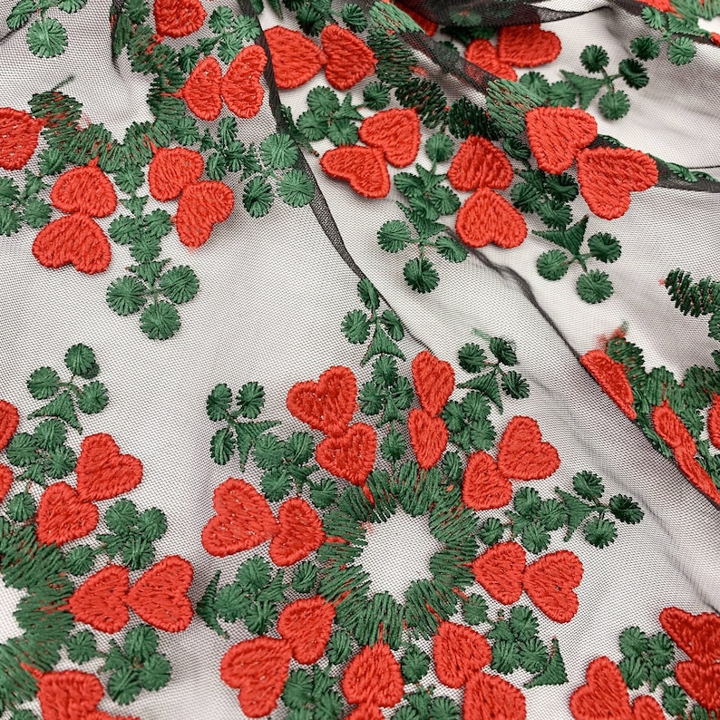 May include: Black mesh fabric with red heart and green leaf embroidery. The fabric has a delicate, lacy texture.