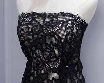 Peut inclure: Robe bustier en dentelle noire sur mannequin. La robe présente des motifs floraux complexes et un bord festonné délicat. La dentelle est superposée à un tissu plus clair, créant un contraste. Petits accents de perles visibles.