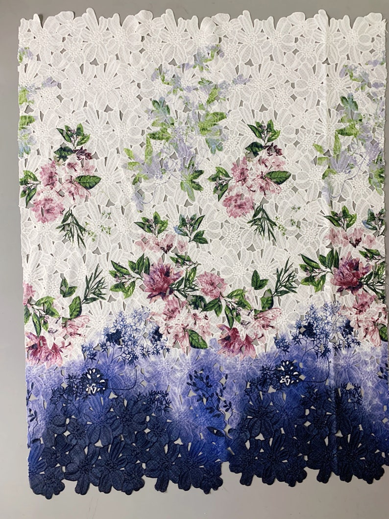 以下が含まれることがあります： ピンク、グリーン、ブルーの色の花柄がプリントされた白いレース生地。生地の下部はブルーのグラデーションになっています。