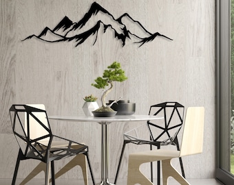May include: Black metal mountain range wall art with a minimalist design. The art is displayed above a white table with two black and white chairs and a small bonsai tree.