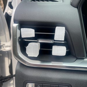 May include: Close-up of a car's interior with a black dashboard and silver trim. There are five white square air fresheners placed in the air vents. The dashboard has buttons labeled "Mode", "AWD", "Auto Hold", and a knob for adjusting the temperature.
