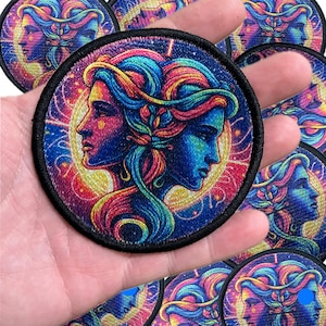 May include: A set of colorful embroidered iron-on patches featuring two faces with intricate details. The faces are surrounded by a swirling galaxy-like background with stars and planets. The patches are circular and have a black border.