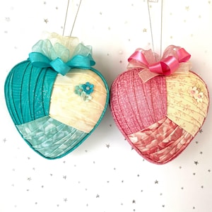 May include: Two heart-shaped ornaments with fabric patchwork. One is teal, cream, and light blue, the other is pink and cream. Both have decorative bows and floral embellishments. These ornaments are perfect for Valentine's Day or other special occasions.