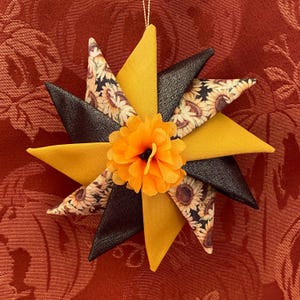 May include: A yellow and black fabric starburst ornament with a sunflower print and a large orange fabric flower in the center.