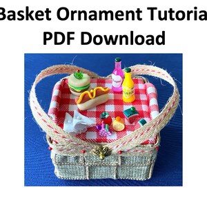 Pode incluir: Um ornamento de cesta de piquenique em miniatura com um pano xadrez vermelho e branco dentro. A cesta est&aacute; cheia de itens de comida e bebida em miniatura, incluindo um cachorro-quente, um hamb&uacute;rguer, fatias de melancia, um lim&atilde;o, uvas e duas garrafas de suco. A cesta &eacute; feita de material tecido e tem uma al&ccedil;a marrom.