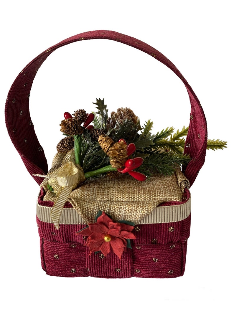 Pode incluir: Uma pequena cesta de Natal vermelha e dourada com al&ccedil;a. A cesta est&aacute; cheia de um ramo de pinho verde e marrom com bagas vermelhas e uma fita dourada.
