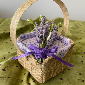 Pode incluir: Uma pequena cesta quadrada de juta com uma fita roxa e um buqu&ecirc; de flores de lavanda. A cesta tem uma al&ccedil;a de juta e &eacute; decorada com contas brancas.