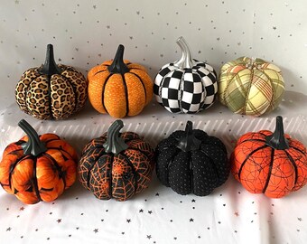 May include: A collection of eight decorative pumpkins with various patterns and textures. The pumpkins feature designs such as leopard print, orange ridges, black and white checkerboard, plaid, spiderwebs, and solid black. Each pumpkin has a dark stem.