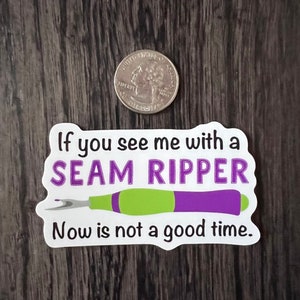 May include: White sticker with the text "If you see me with a SEAM RIPPER Now is not a good time."  A purple and green seam ripper is illustrated below the text.