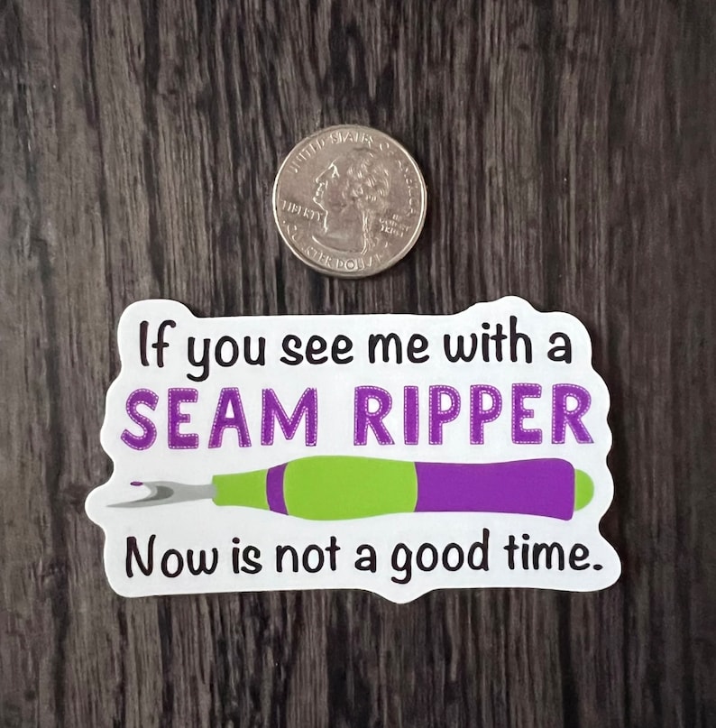 May include: White sticker with the text "If you see me with a SEAM RIPPER Now is not a good time."  A purple and green seam ripper is illustrated below the text.
