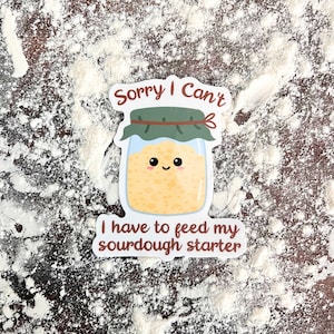 May include: A white sticker with a cartoon illustration of a jar of sourdough starter with a smiling face. The text on the sticker reads "Sorry I Can't I have to feed my sourdough starter."