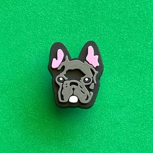 May include: A black and gray French bulldog charm with pink ears. The charm is made of rubber and has a glossy finish.