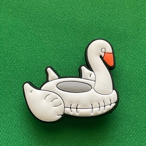 May include: White inflatable swan pool float charm. The charm is made of rubber and has a black outline. The swan has a small orange beak.