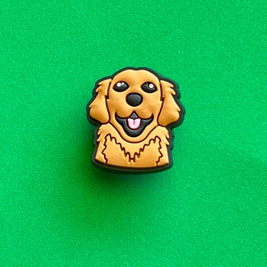 May include: A golden retriever dog charm with a black outline. The dog is smiling with its tongue sticking out.
