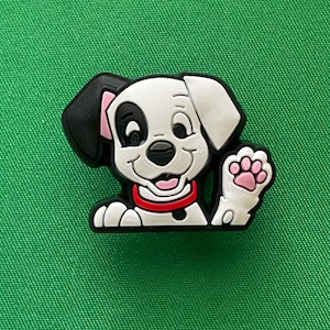 May include: A white and black Dalmatian dog cartoon charm with a pink paw raised in a wave. The dog is wearing a red collar.