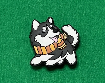 May include: A black, white, and gray husky dog charm with a brown and yellow scarf. The charm has a black border and is on a green background. The dog is sticking its tongue out.