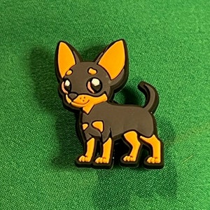 May include: A black and orange cartoon chihuahua charm with big eyes. The charm is made of rubber and is about 2 inches tall.