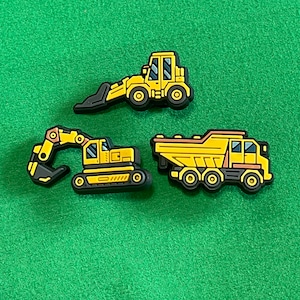 May include: Three yellow toy construction vehicles: a dump truck, an excavator, and a front loader. The vehicles are made of plastic and have black wheels.