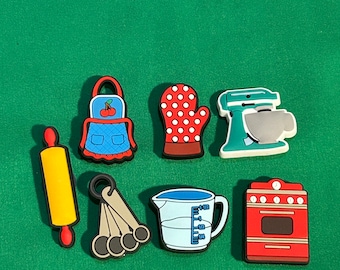 Könnte beinhalten: Ein Set aus acht bunten Küchen-Charm aus Silikon, darunter eine rote und blaue Schürze, ein roter und weißer Ofenhandschuh, ein gelber Nudelholz, ein Satz mit vier silbernen Messlöffeln, ein blauer Messbecher, eine rote und weiße Küchenmaschine und ein roter Herd.