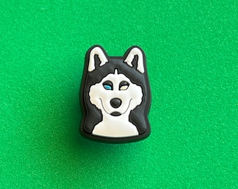 May include: A black and white husky dog charm with blue and yellow eyes. The charm is made of rubber and has a 3D design.