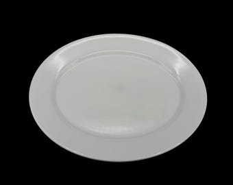 May include: A plain, circular white ceramic dinner plate with a smooth, glossy finish and a wide, flat rim. The plate features a simple, clean design with a slightly recessed center and a uniform, solid white color throughout the entire surface.