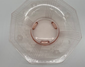 May include: A pink glass serving dish with an octagonal shape and a floral design. The dish has three small feet and is made of clear glass with a pink tint.