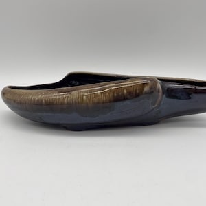 May include: A ceramic planter with a glossy finish. The planter is a dark blue color with a brown rim. The planter has a unique, elongated shape, perfect for displaying small plants or succulents.