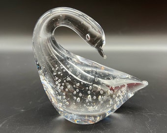 May include: A clear glass swan figurine with a textured surface and air bubbles throughout. The swan's neck is curved and its head is tilted down.